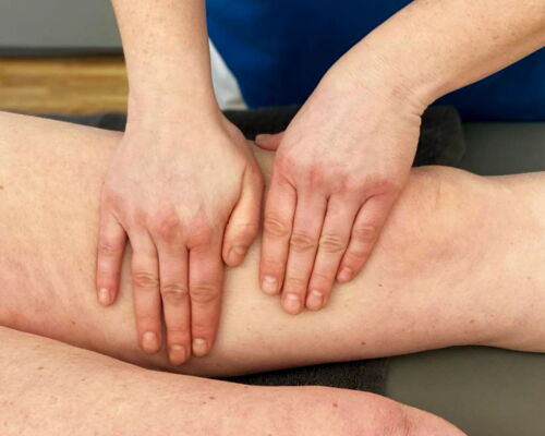 Zwei Hände massieren den Oberschenkel eines Patienten.