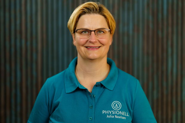 Physiotherapeutin Julia Neelsen sitzt draußen mit den Rücken angelehnt an ihrem Praxisschild.